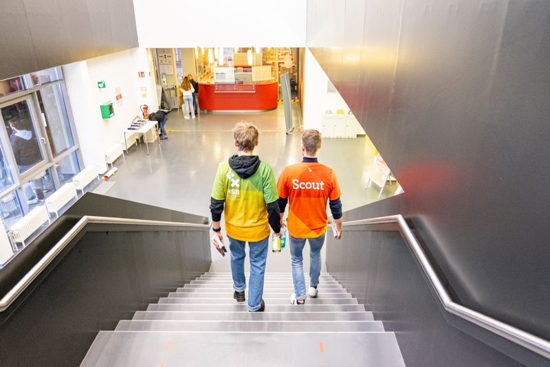 Eine Aufnahme von oben wie zwei Studenten eine Treppe herunterlaufen. Sie tragen T-Shirts mit einem HSB-Logo und der Aufschrift "Scout".