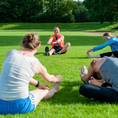 RS4844__DSC653520170704.jpg Eine Personengruppe sitzt im Kreis auf der Wiese und dehnt sich.