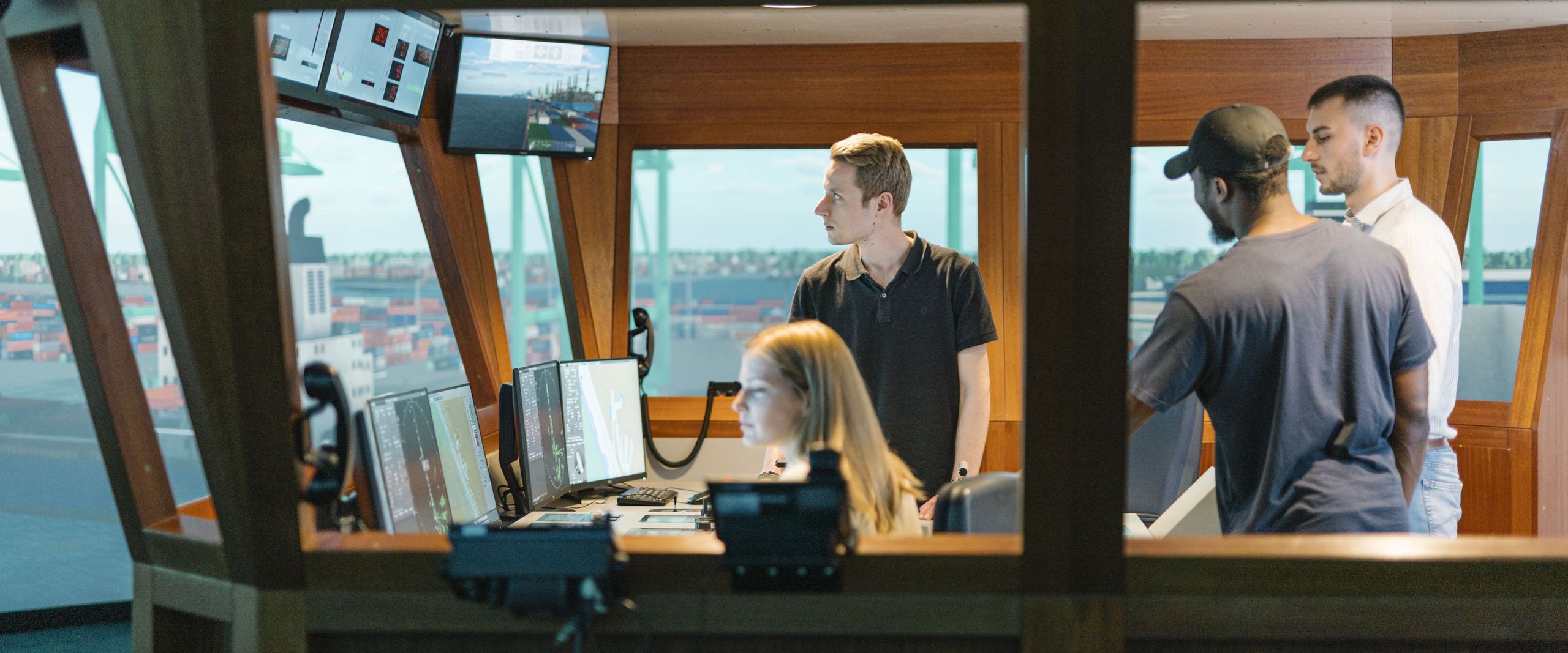 Junge Männer und eine Frau sitzen und arbeiten in einem Schiffssimulator.