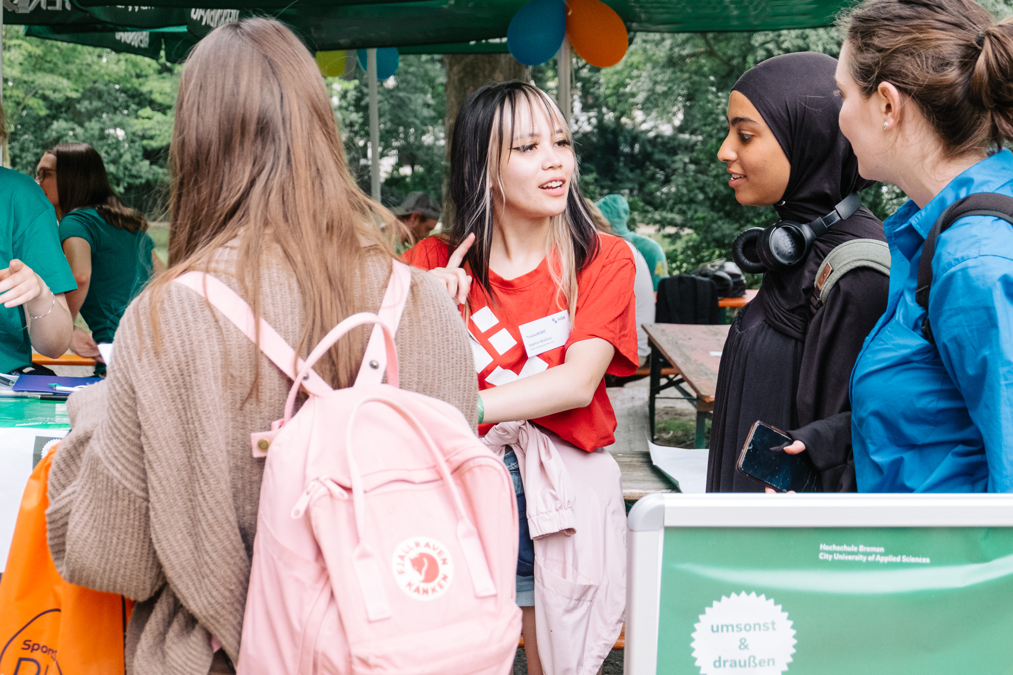 3 Studentinnen melden sich bei einer Hilfskraft für das Sommerfest an. 