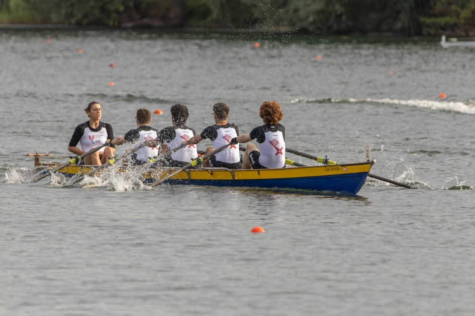 Vier Ruderer sitzen gemeinsam während der Deutschen Hochschulmeisterschaft Rudern in einem Boot. Vor ihnen sitzt eine Steuerfrau