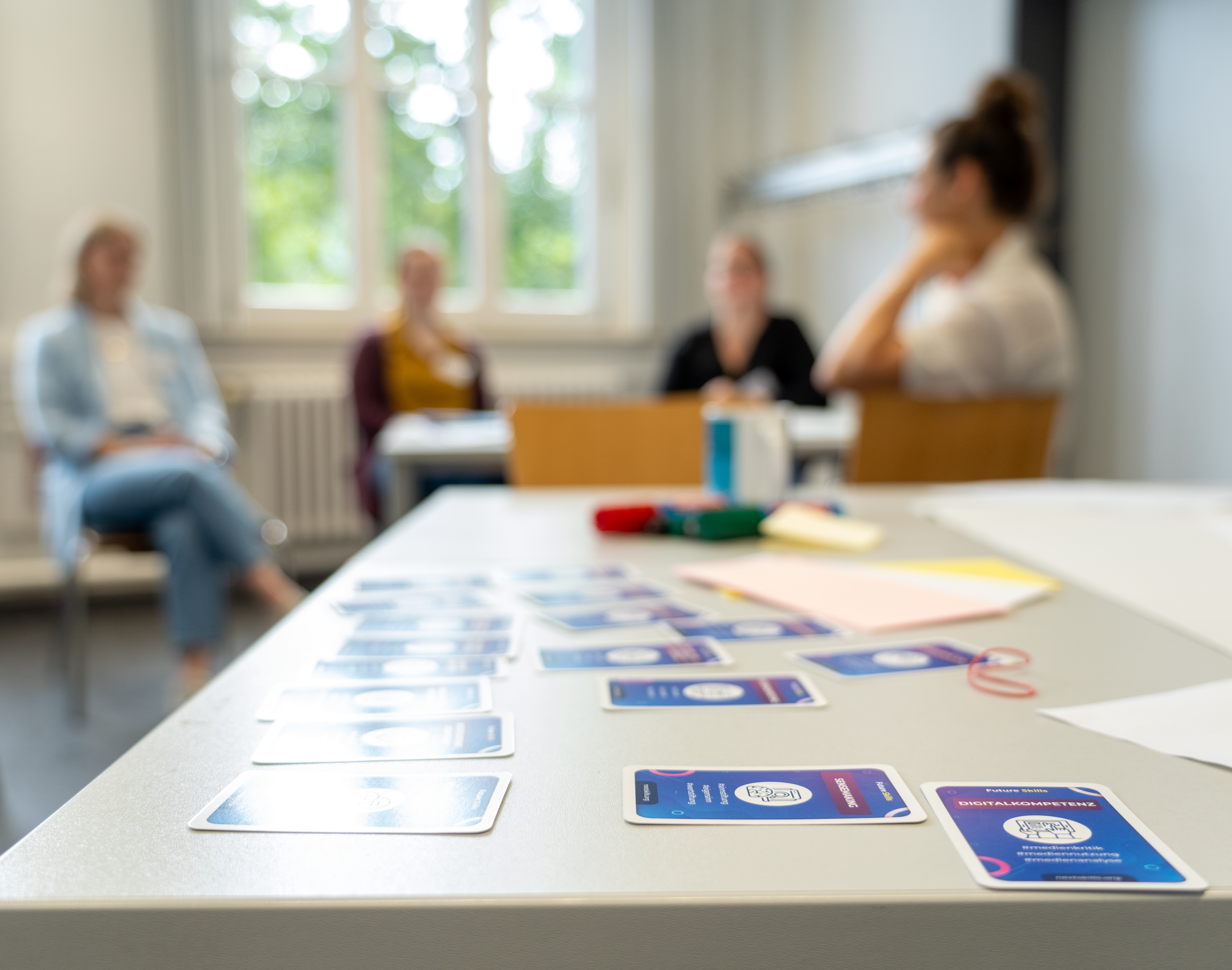 Gesprächssituation in einem Seminarraum: Vier Personen sitzen zusammen, auf dem Tisch liegen Moderationskarten und Materialien.