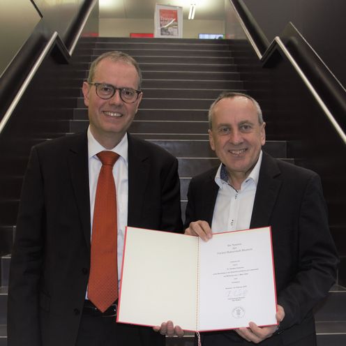 Zwei M&auml;nner halten eine Urkunde und l&auml;cheln in die Kamera