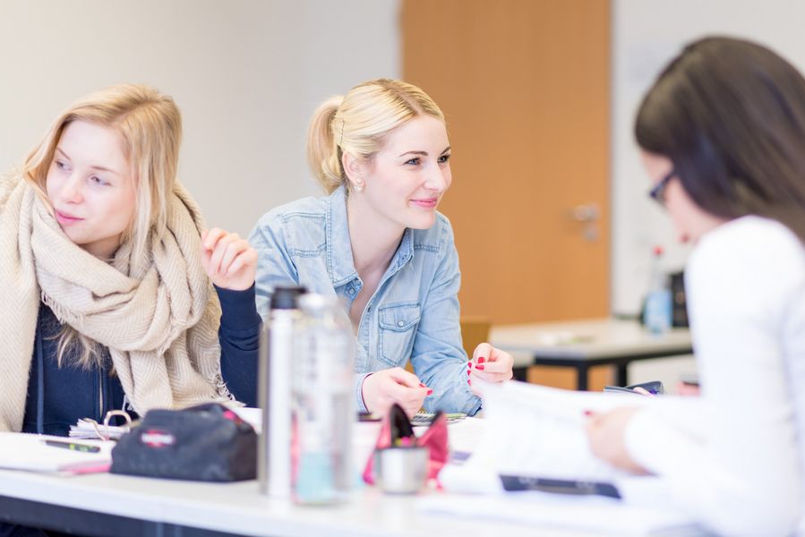 Studierende sitzen in einem Vorlesungsraum und unterhalten sich.