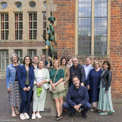 Gruppenbild mit M&auml;nnern und Frauen an der Skulptur der Bremer Stadtmusikanten. 