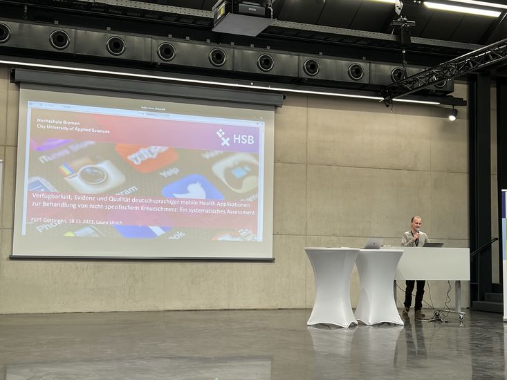 Student Lauro Ulrich stellt seine Thesis beim Forschungssymposium Physiotherapie vor. Er steht an einem Rednerpult vor einer Leinwand