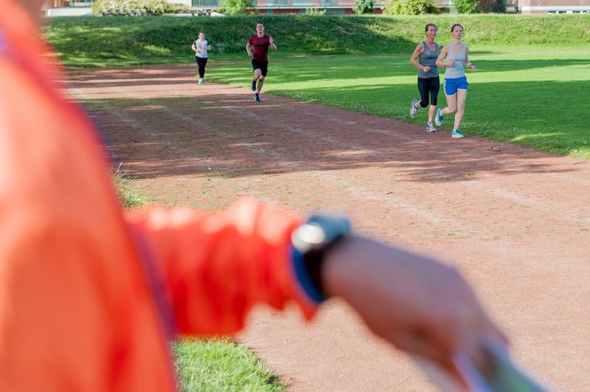 Läufer auf der Strecke und im Vordergrund ein Arm mit einer Armbanduhr.
