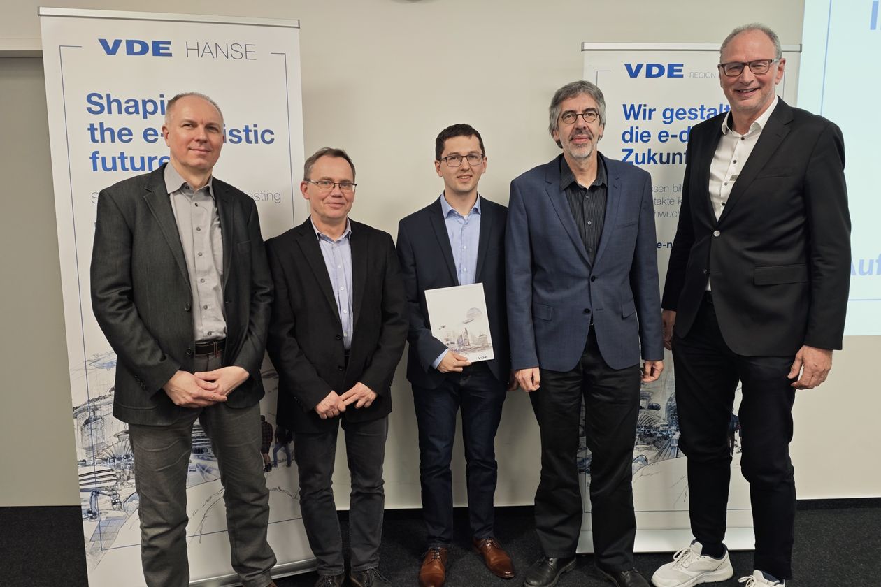 Gruppenbild mit Männern im Anzug, die vor Roll-ups stehen. Einer in der Mitte hält eine Urkunde.