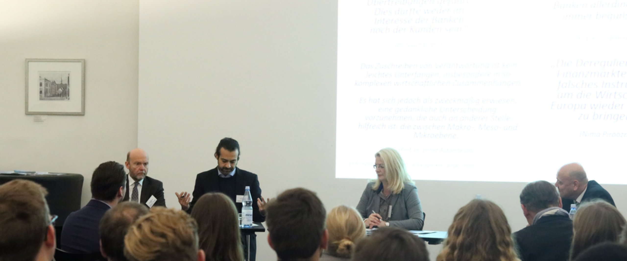 EFA-Symposium Männe rund Frauen sitzen in einem Raum und diskutieren. Hinter ihnen ist eine Powerpointpräsentation.