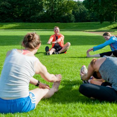 Eine Personengruppe sitzt im Kreis auf der Wiese und dehnt sich.