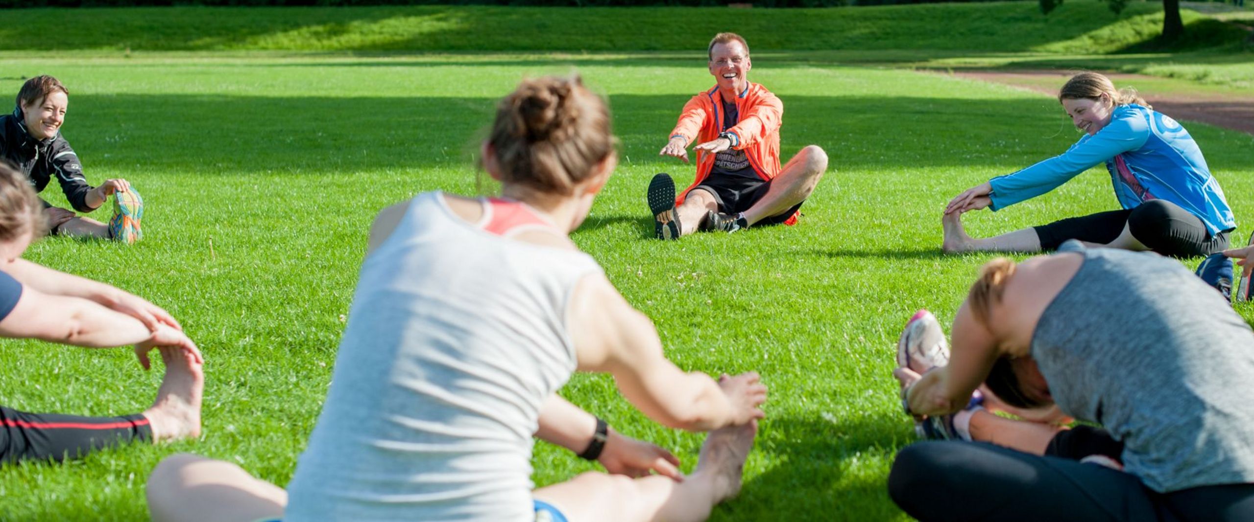 Eine Personengruppe sitzt im Kreis auf der Wiese und dehnt sich.