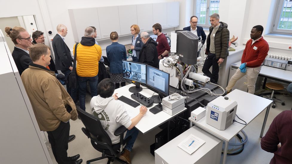 Laboratory with equipment. Numerous men and women look around.