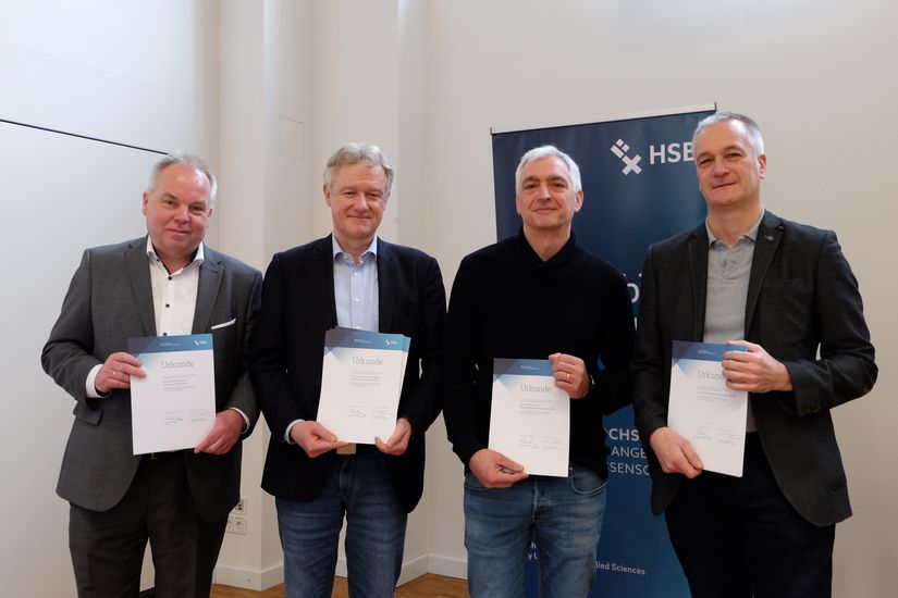 Vier M&auml;nner halten Urkunden und l&auml;cheln in die Kamera.