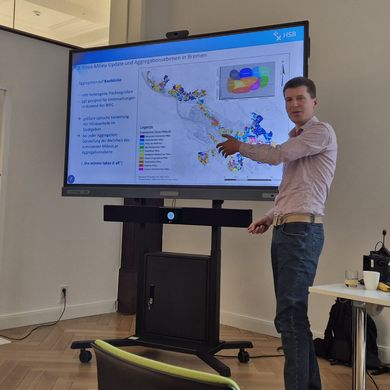 Timmy Schwarz präsentiert Forschungsergebnisse vor einem großen Monitor 