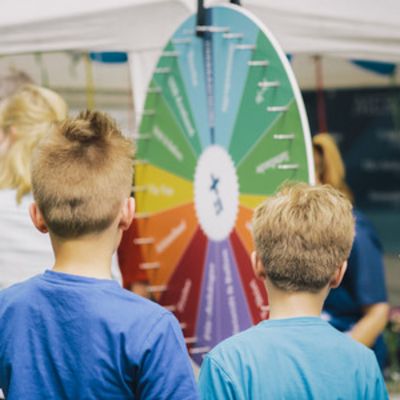 Kinder Mittig fokussiert im Vordergrund stehen zwei Kinder. Die Kinder sind nur von Hinten zu sehen Oberkörper aufwärts. Die Kinder blicken auf ein Drehrad im Hintergrund.