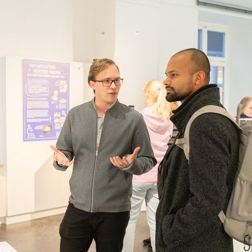 Auf dem Bild sind zwei M&auml;nner zu sehen, die vor einer Glasvitrine mit einem Modell stehen und sich unterhalten. 