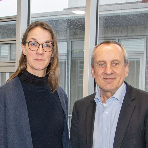 Bild einer Frau und einem Mann, die vor einer Fensterfront stehen. Beide l&auml;cheln in die Kamera.