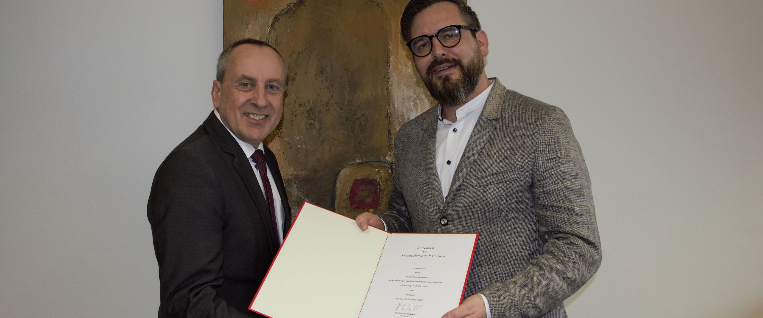 Ernennung Kay Suwelack Zwei Männer halten eine Urkunde und lächeln in die Kamera