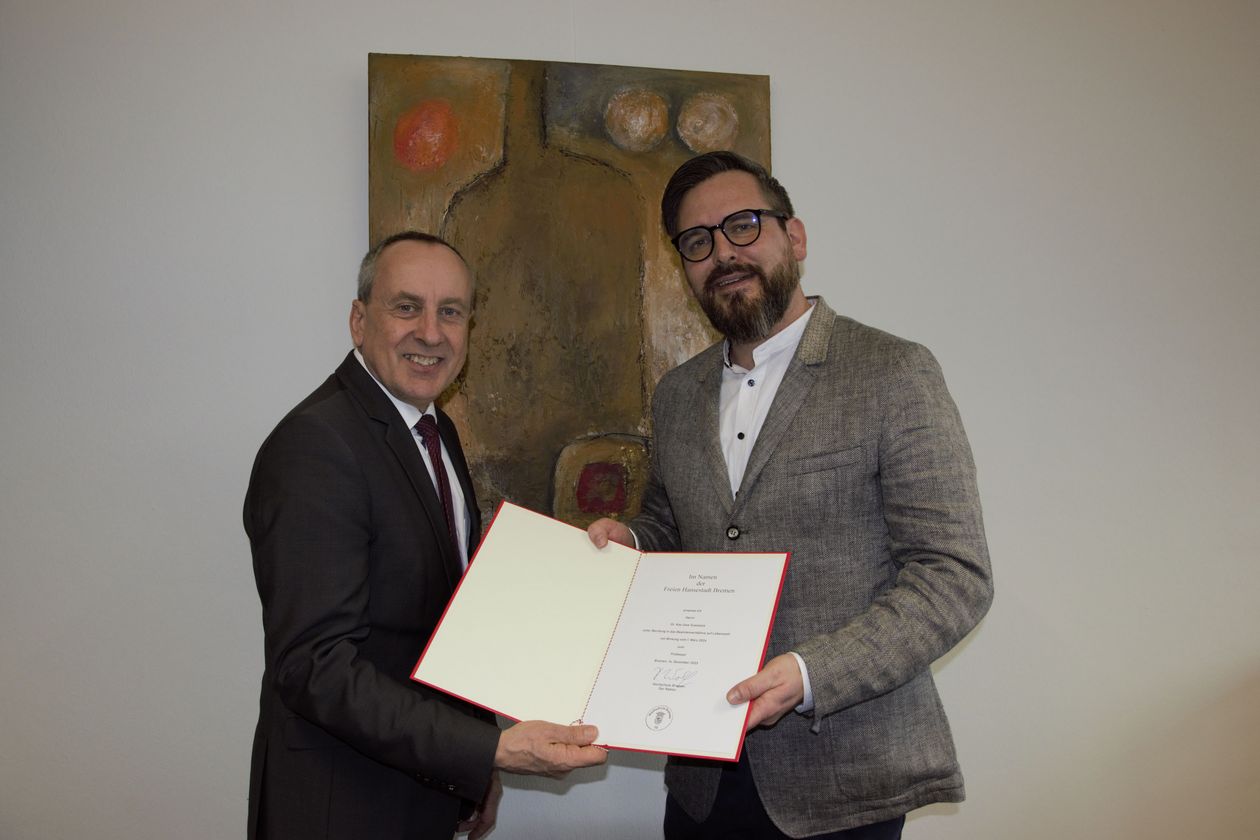 Zwei Männer halten eine Urkunde und lächeln in die Kamera