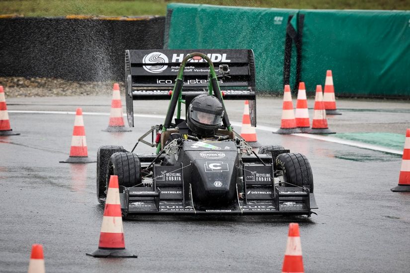 Auf dem Bild fährt der von Studierenden der Hochschule Bremen (HSB) und Universität Bremen entwickelte Rennwagen über eine Teststrecke. Neben dem Rennwagen stehen zur Begrenzung der Strecke mehrteilige Leitkegel.