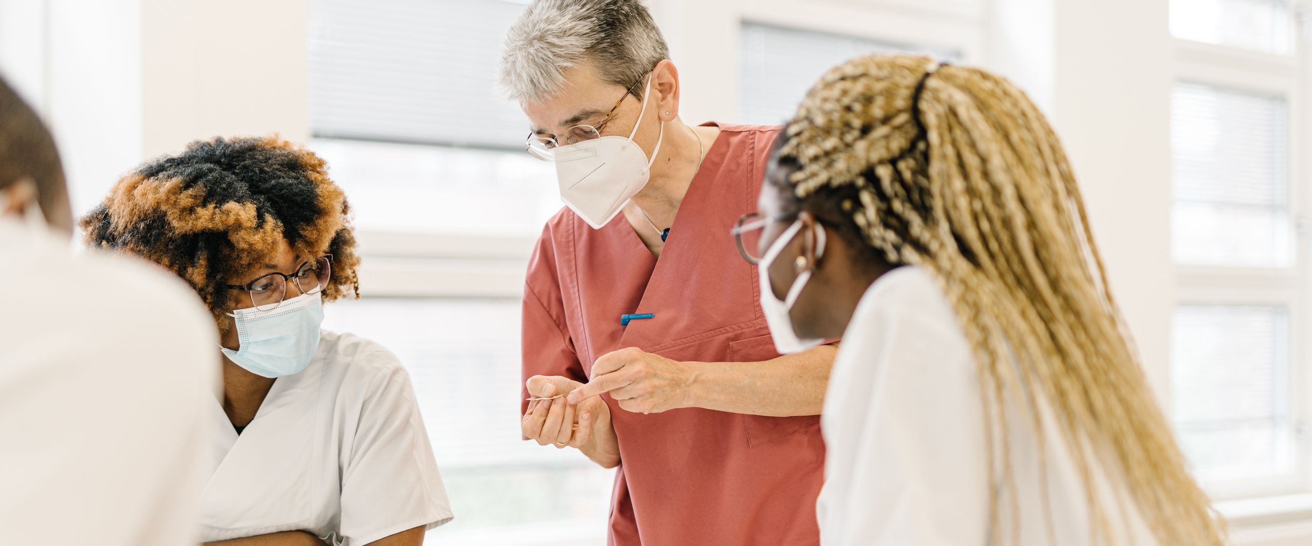 Pflege HSB Menschen stehen an einem Tisch und besprechen sich. Sie haben zum Teil weiße Kittel an.