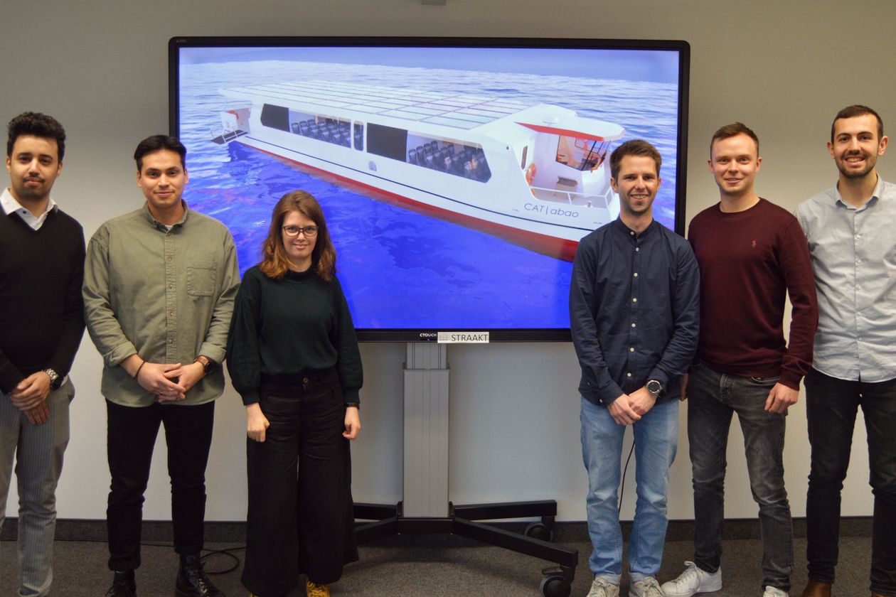 Gruppenbild mit sechs jungen M&auml;nnern und einer jungen Frau. Hinter ihnen ist auf einem Beamer das Modell ihrer konzipierten F&auml;hre zu sehen.