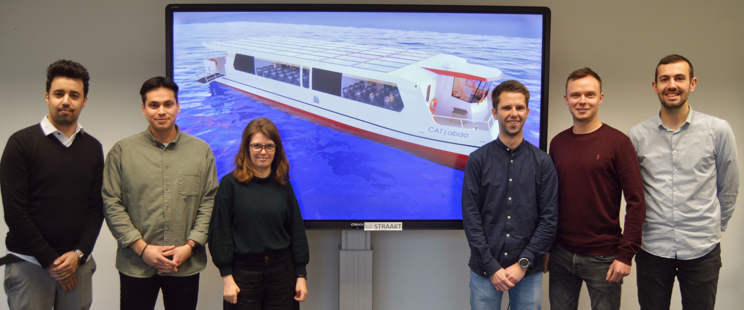 Gruppenbild mit sechs jungen M&auml;nnern und einer jungen Frau. Hinter ihnen ist auf einem Beamer das Modell ihrer konzipierten F&auml;hre zu sehen.