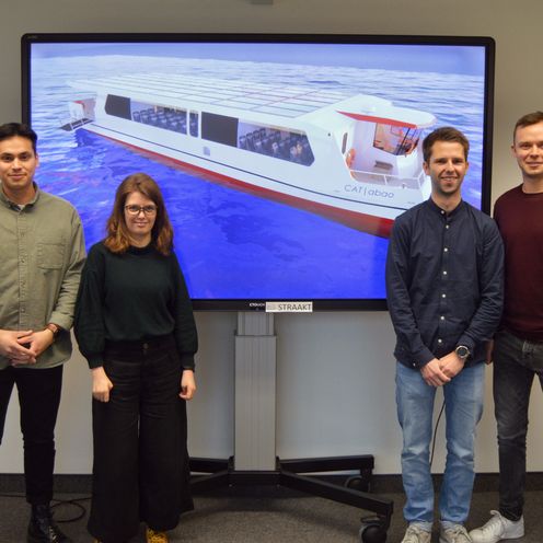 Gruppenbild mit sechs jungen M&auml;nnern und einer jungen Frau. Hinter ihnen ist auf einem Beamer das Modell ihrer konzipierten F&auml;hre zu sehen.