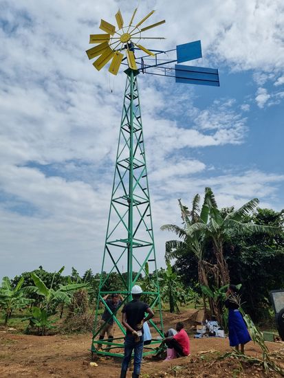  windkraftbetriebene Wasserpumpe auf einem Feld. Davor sind menschen