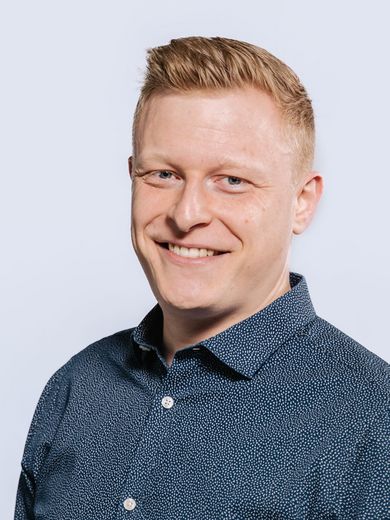 Auf dem Bild ist Manuel Schäfer zu sehen. Er hat blondes kurzes Haar und trägt ein blaues Hemd. 