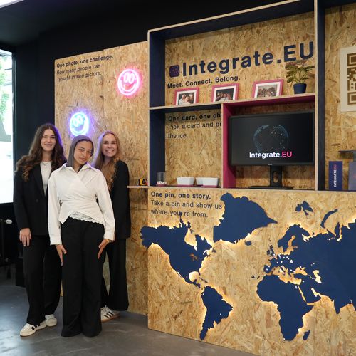 Three young women are standing in front of a display featuring a map and shelving units