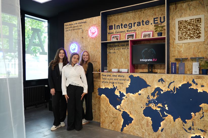 Three young women are standing in front of a display featuring a map and shelving units