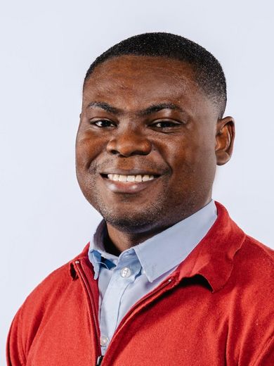 Auf dem Foto ist Antoine Eyram Kwame zusehen. Er hat kurzes schwarzes Haar und trägt ein blaues Hemd unter einem roten Pullover. 
