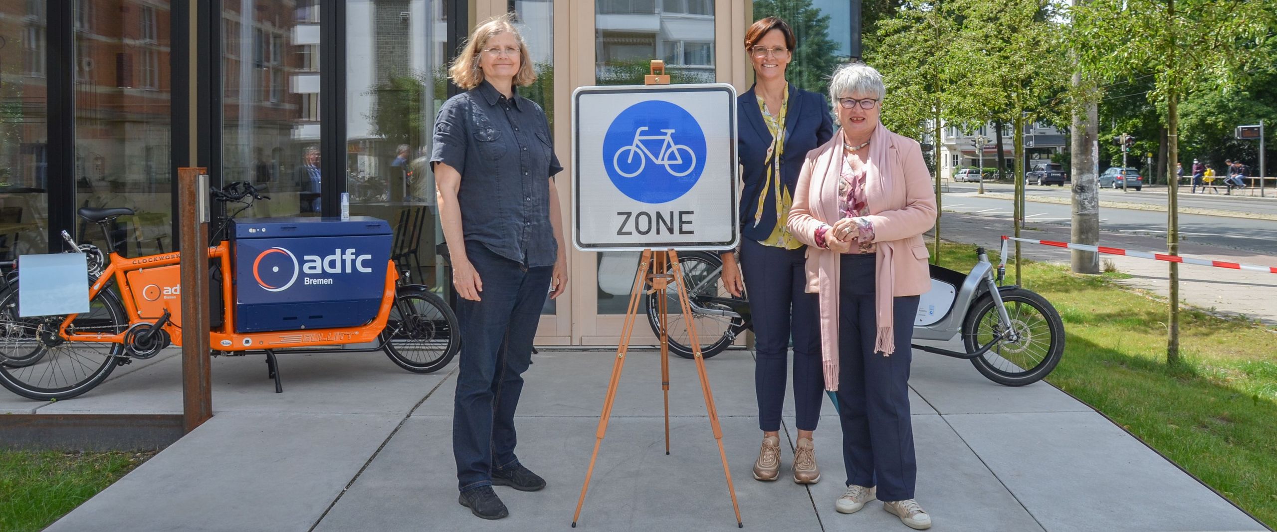 Steffi Kollmann, Ulrike Mansfeld und Karin Luckey stehen neben einem Schild "Fahrradzone" vor dem FahrradRepaircafé.