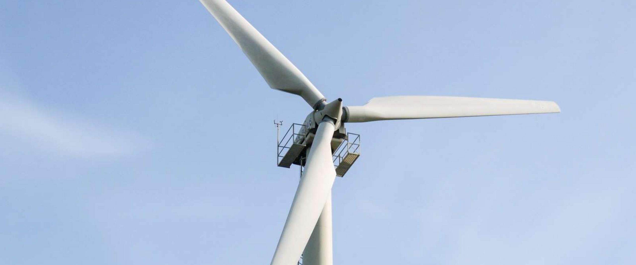 Auf dem Bild ist der obere Teil einer Windkraftanlage zu sehen. Im Hintergrund ist blauer Himmel. 
