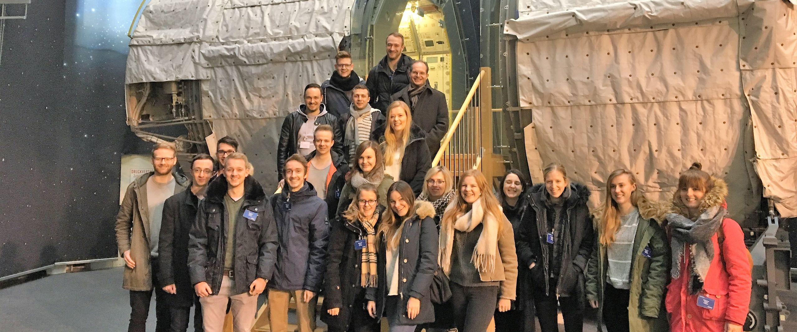 Eine Gruppe Studierender steht vor Bauteilen einer Rakete.