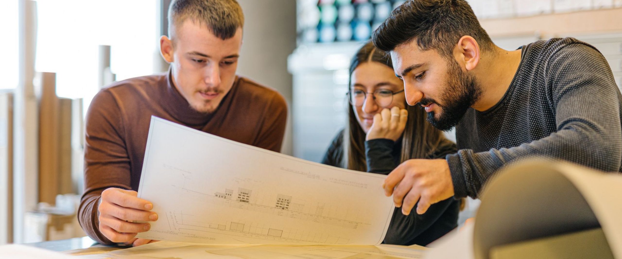 Drei Studierende betrachten einen Bauplan 