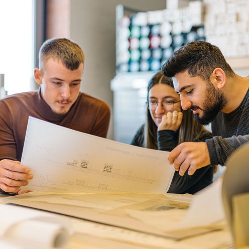 Drei Studierende betrachten einen Bauplan 