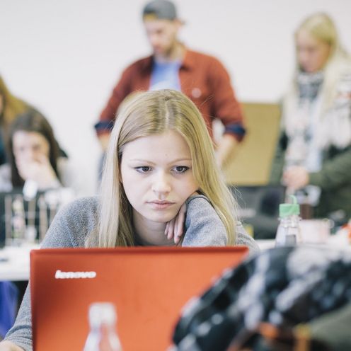 Studentin im vollen Vorlesungsraum vor einem Laptop.