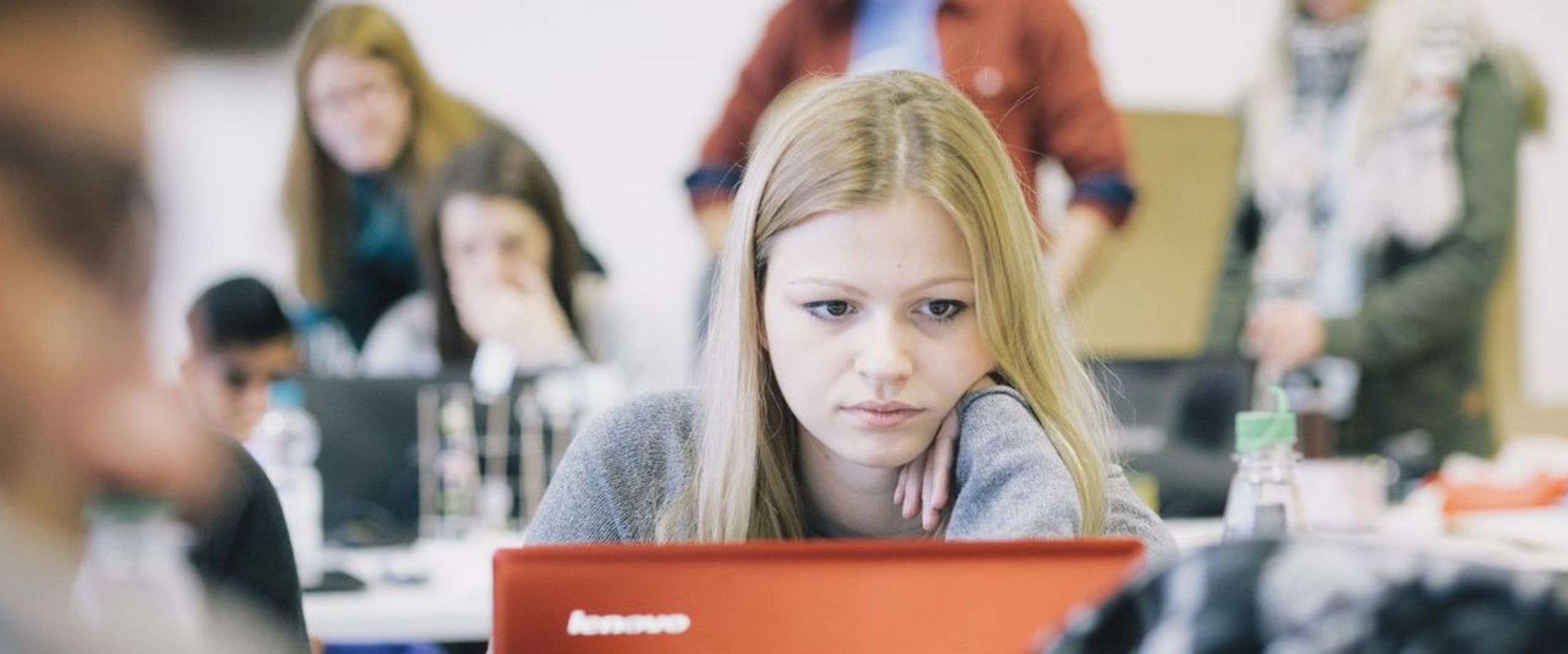 Studentin im vollen Vorlesungsraum vor einem Laptop.