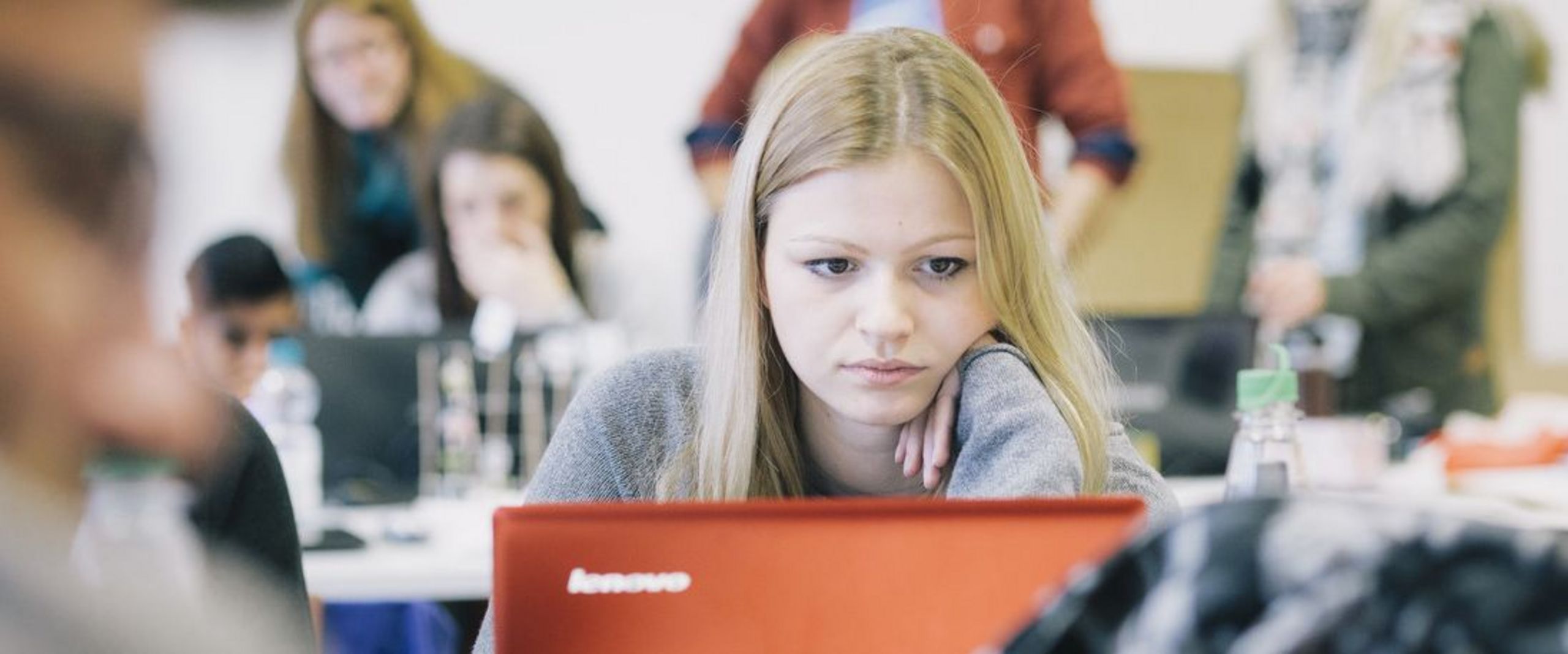 Studentin im vollen Vorlesungsraum vor einem Laptop.