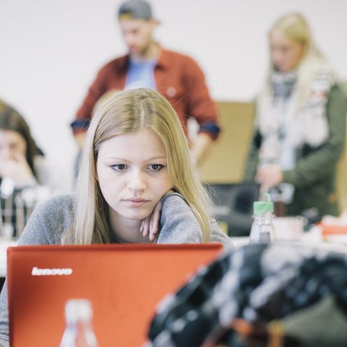 Studentin im vollen Vorlesungsraum vor einem Laptop.
