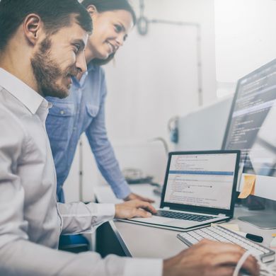 Mann und Frau schauen gemeinsam auf mehrere Computerbildschirme