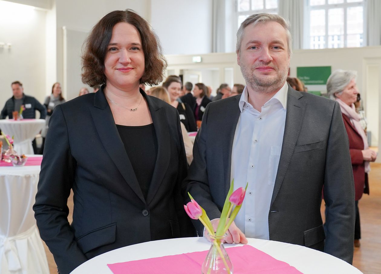 Bild von Frau und Mann an Stehtisch. Beide l&auml;cheln in die Kamera.