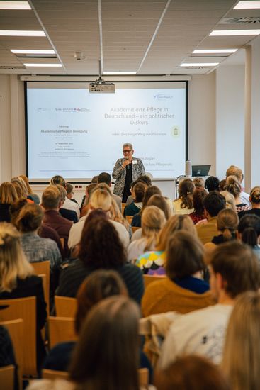 Christine Vogler, Präsidentin des Deutschen Pflegerats und Geschäftsführerin des Berliner Bildungscampus für Gesundheitsberufe, steht bei ihrem Vortrag vor einer Leinwand.