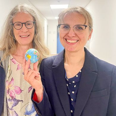 Zwei Frauen lachen in die Kamera. die rechte h&auml;lt eine kleine Weltkugel.