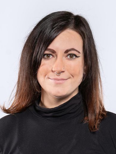 Auf dem Foto ist Kelly Mainwaring zusehen. Sie hat schwarze schulterlange Haare und tr&auml;gt einen schwarzen Rollkragenpullover.