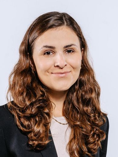 Auf dem Foto ist Katrin Winkler zusehen. Sie hat braune lockige Haare und trägt ein Beiges T-Shirt unter einem schwarzen Blazer. 