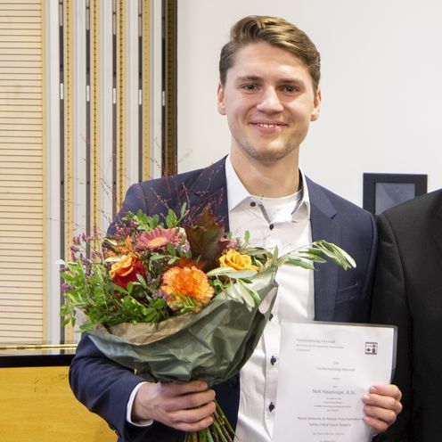 Gruppenbild mit 4 Personen (zwei Männern und einer Frau). Der Mann ganz links hat einen Blumenstrauß in der Hand. Alle lachen in die Kamera.