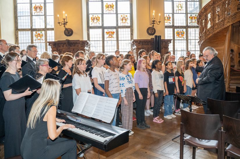 Chor mit Erwachsenen und Kindern sowie Pianospielerin und Dirigent